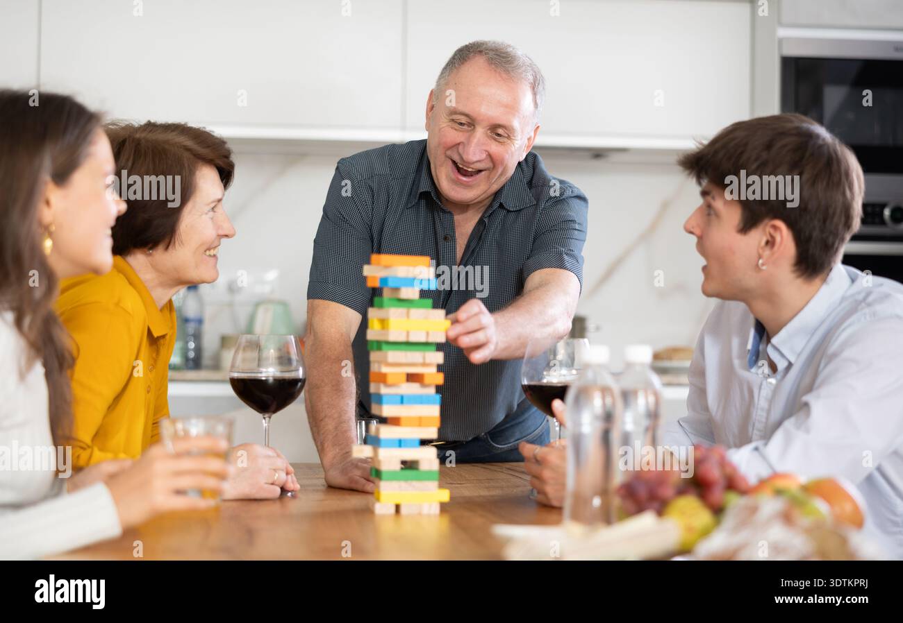 Un anziano sorridente o un padre che si divertono a giocare nella costruzione della torre con la moglie e i bambini adulti in una comoda casa di famiglia Foto Stock