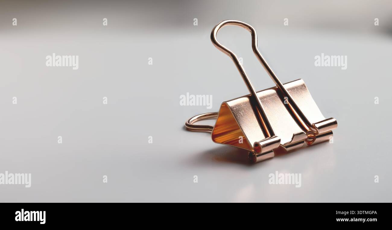 Clip legante in oro rosa metallizzato posizionata su una superficie neutra con ampio spazio per le copie Foto Stock