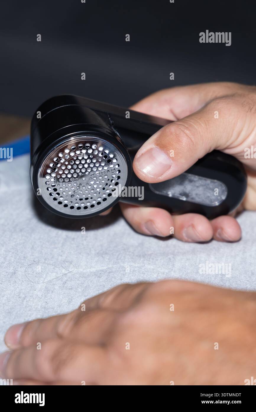 Una persona tiene in mano uno strumento di pulizia portatile progettato per rimuovere lanugine e detriti dalle superfici in tessuto. Foto Stock