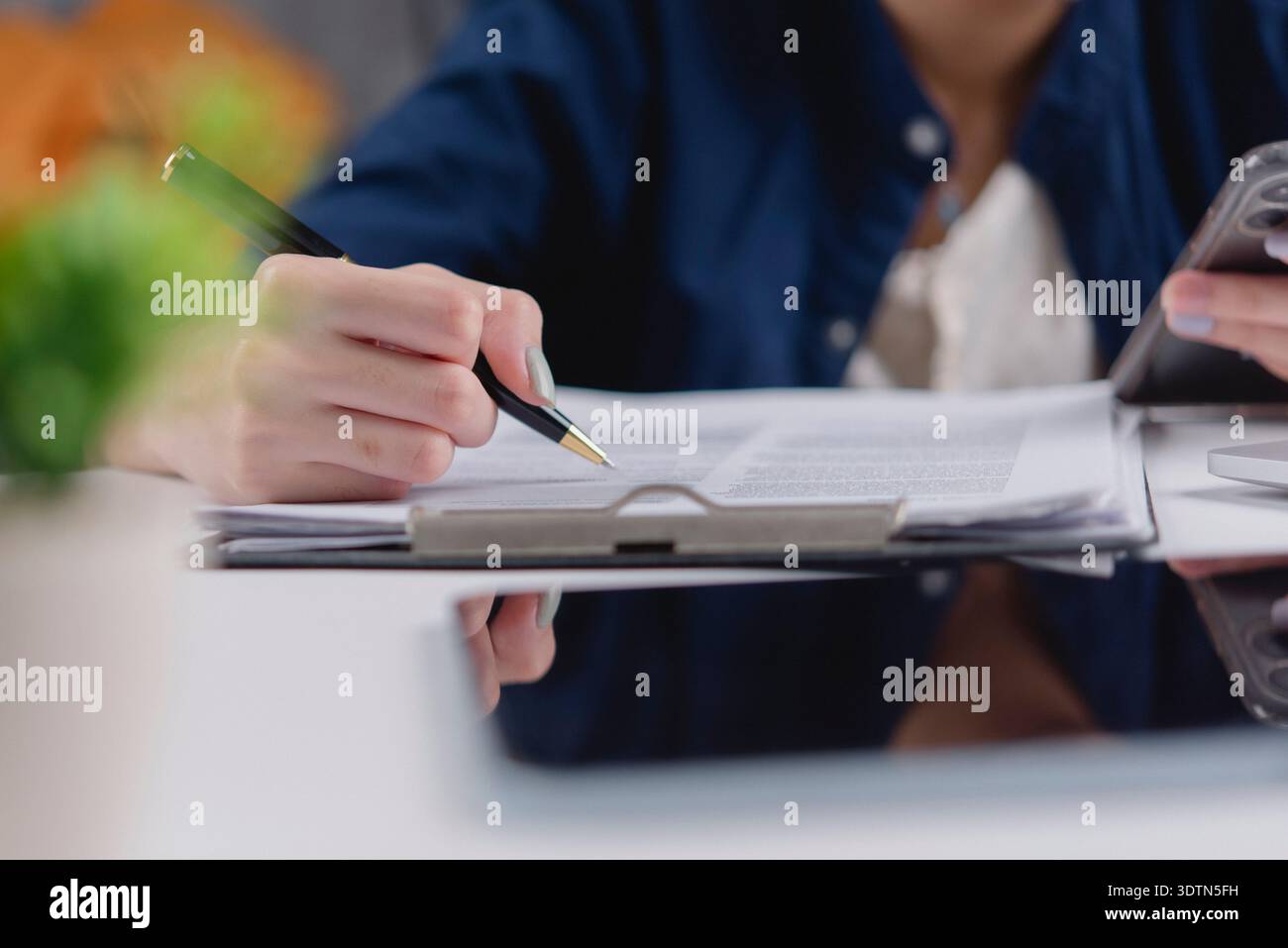 Donna freelance penna a mano che scrive appunti documento, controllare lo smartphone. Multitasking, lavoro da casa, ufficio, scrivania. E-learning per studenti, formazione online. Revisione p Foto Stock