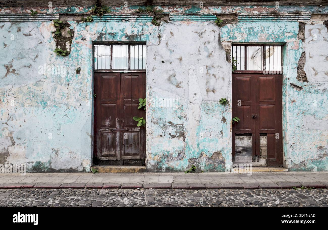 Vintage abbandonato edificio coloniale con porte in legno e piante che crescono fuori dalle pareti fessurate, Antigua, Guatemala Foto Stock