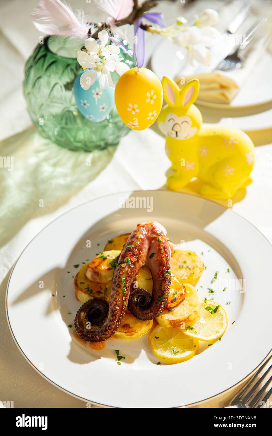 Polpo grigliato gourmet con patate servito su un elegante tavolo di Pasqua. Piatto di pesce natalizio primaverile con decorazioni natalizie Foto Stock