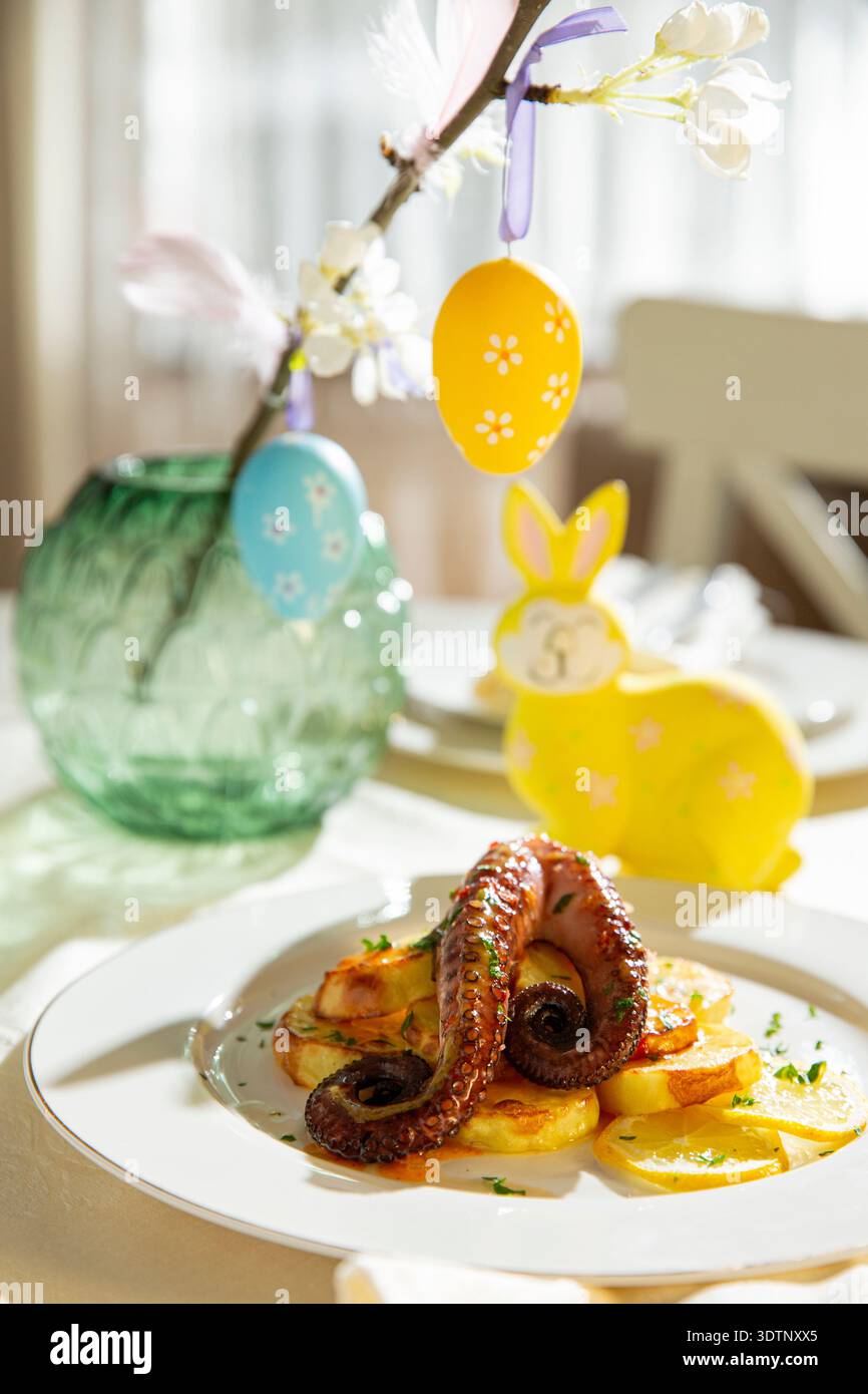 Polpo grigliato gourmet con patate servito su un elegante tavolo di Pasqua. Piatto di pesce natalizio primaverile con decorazioni natalizie Foto Stock