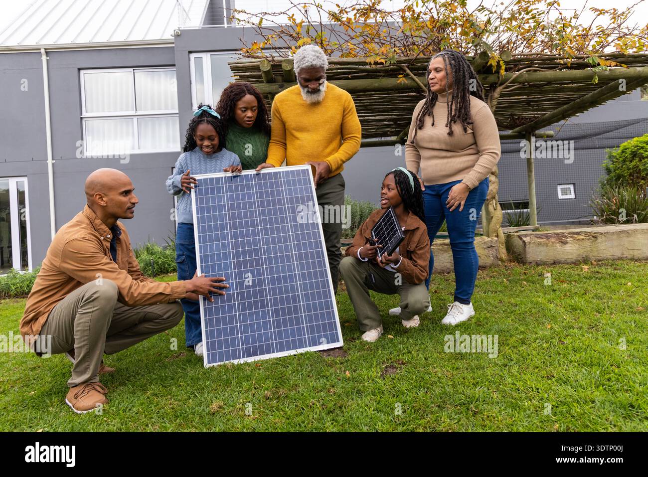 Famiglia afroamericana che esamina un grande pannello solare con un piccolo pannello portatile sul cortile anteriore erboso. Fotovoltaico, array, outdoor, casa, dimostrazione, Foto Stock