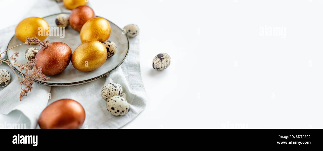 Uova di Pasqua dorate e di bronzo in un piatto grigio su un tovagliolo di lino su sfondo bianco Foto Stock
