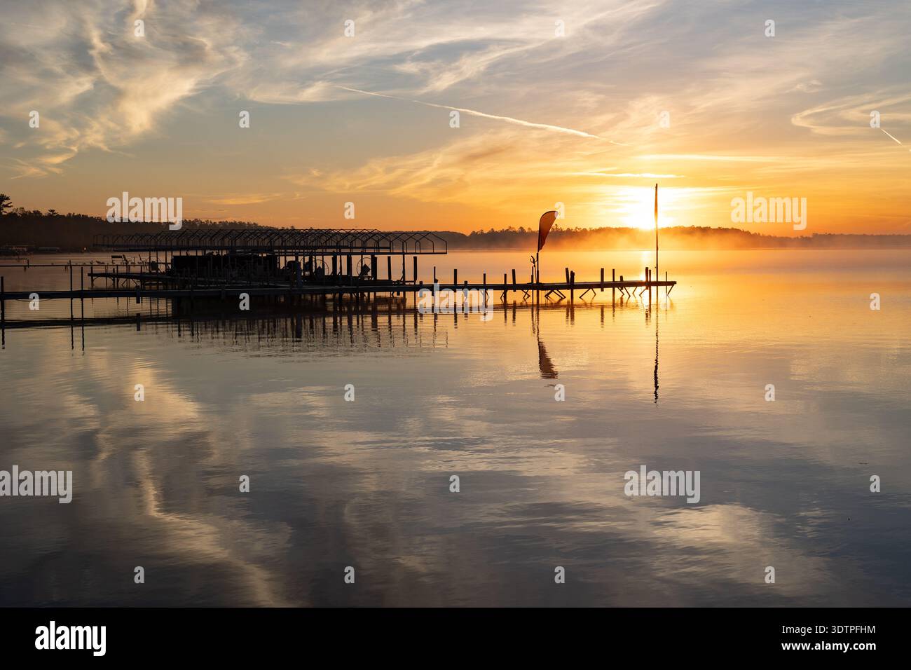 Alba dorata sul lago calmo con molo e riflessi nebbiosi. Foto Stock