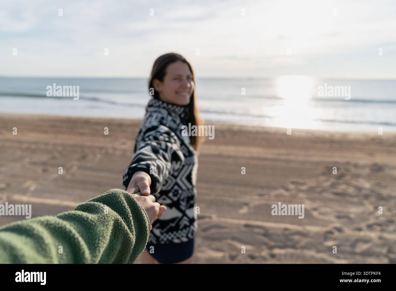 Donna sorridente che tiene la mano sulla spiaggia all'alba Foto Stock