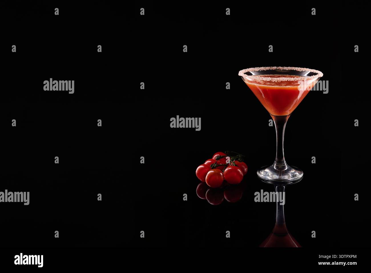 Cocktail di pomodoro rosso in un bicchiere di martini con gamberi di sale e pomodori ciliegini freschi, che si riflettono su una superficie scura e lucida Foto Stock
