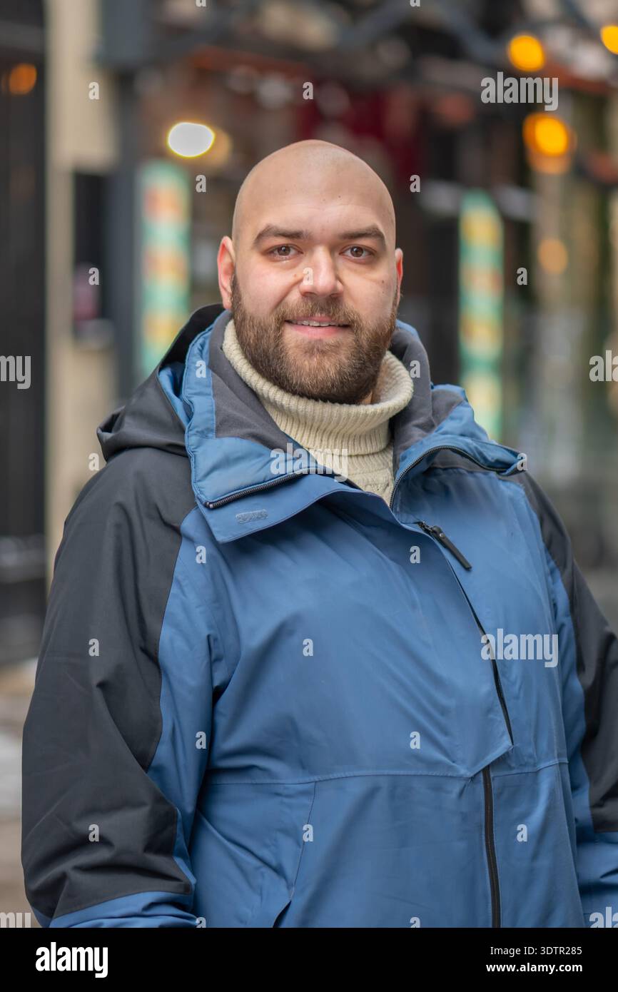 uomo di 35 anni con una giacca calda che cammina lungo una strada della città in inverno Foto Stock