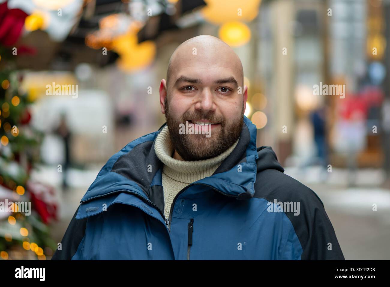 Uomo di 35 anni in piedi su una strada della città vicino all'albero di Natale decorato in inverno Foto Stock
