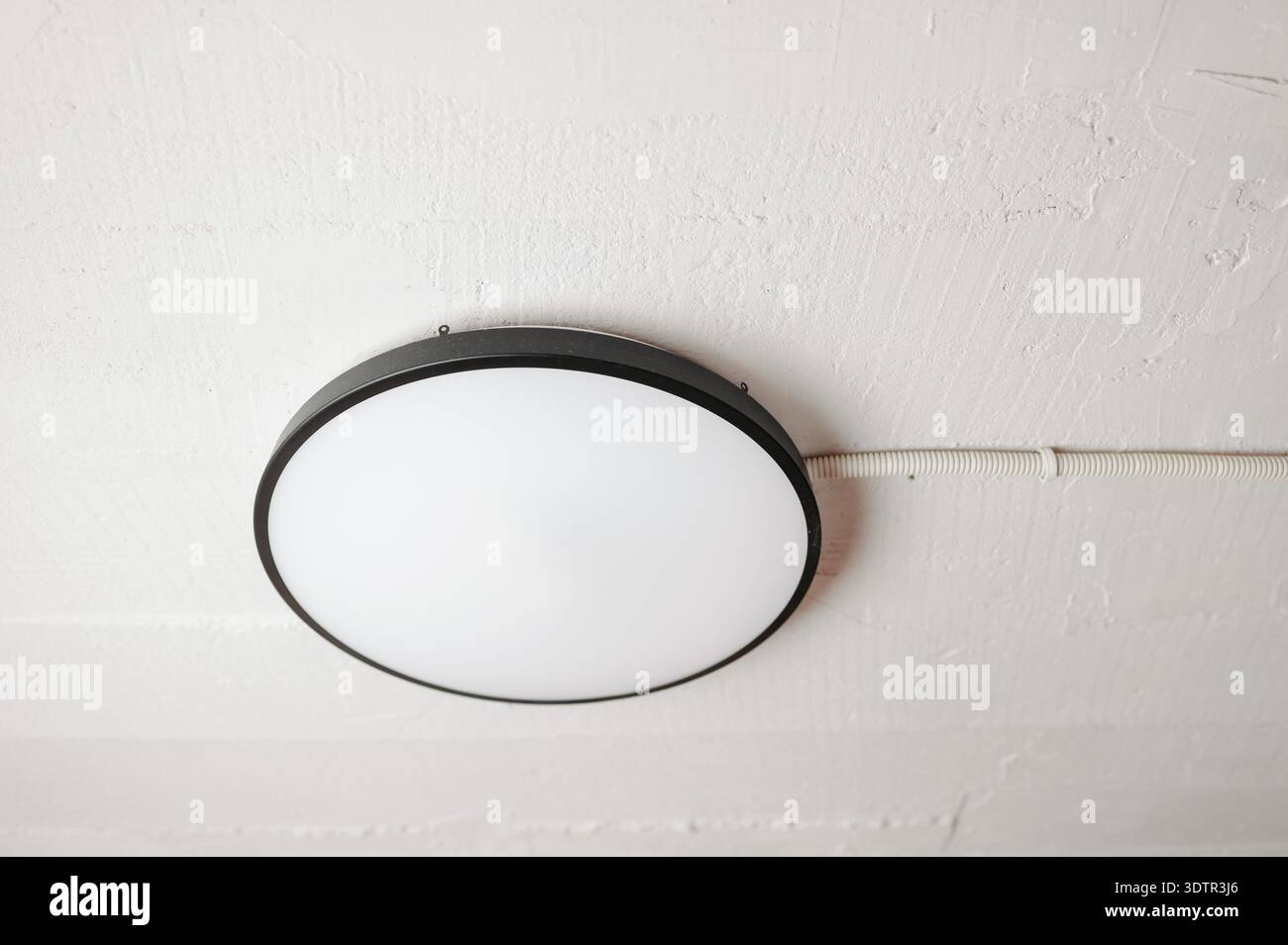 Plafoniera rotonda minimalista con bordo nero opaco e soffice bagliore in uno spazio interno neutro Foto Stock