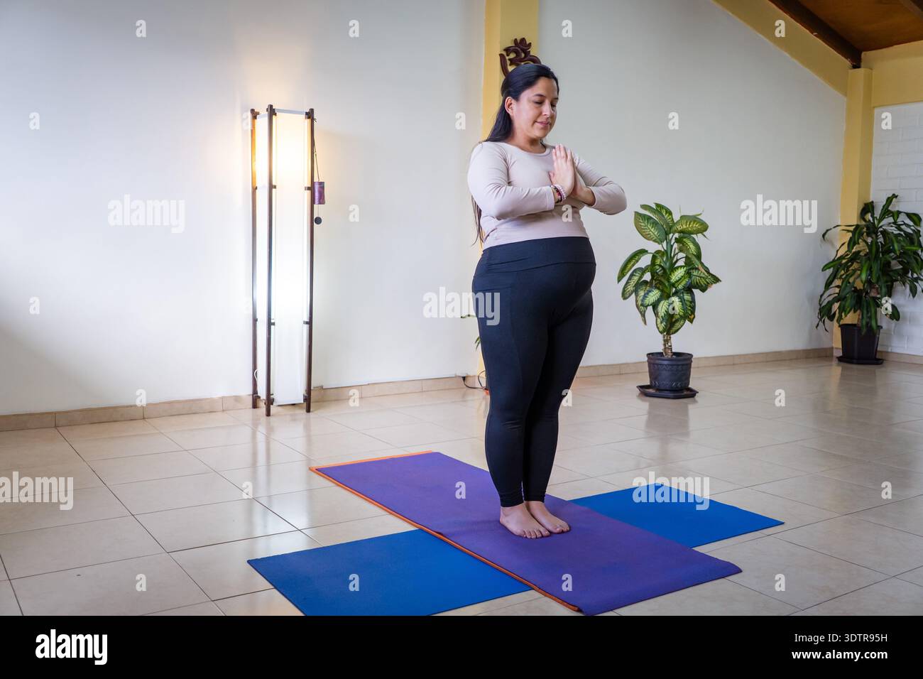 Donna incinta in piedi su un tappetino da yoga con le mani insieme in uno studio Foto Stock