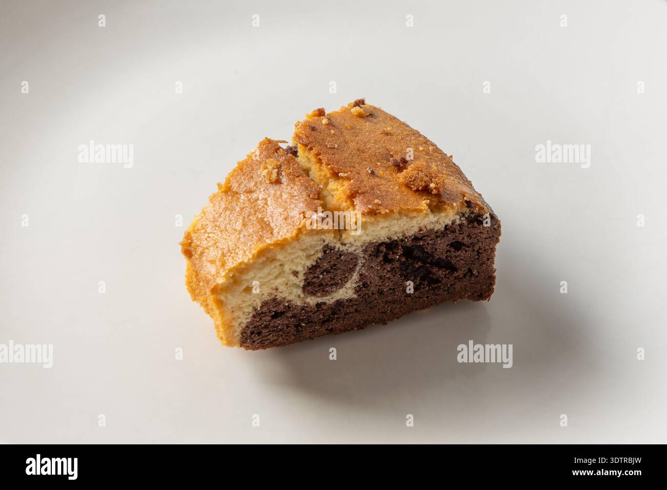 Una fetta di torta di marmo al cioccolato con una consistenza umida e una crosta dorata, elegantemente presentata su un piatto bianco. Foto Stock