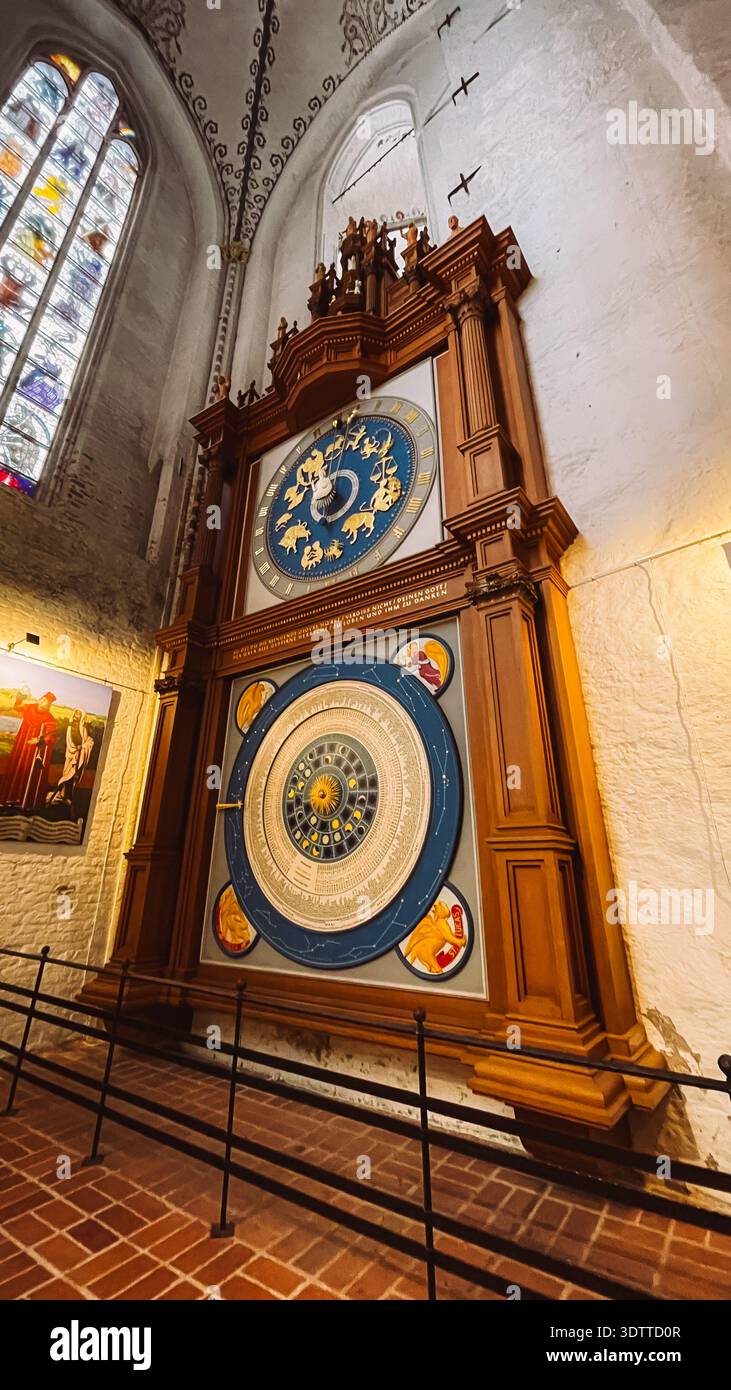 Orologio astronomico con quadrante zodiaco esposto sulla parete della chiesa vicino a vetrate colorate Foto Stock