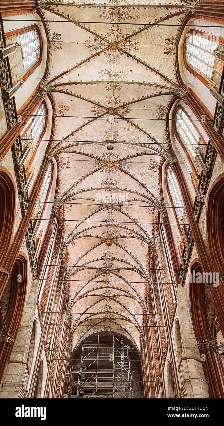 Il soffitto a volta a costola dipinto si estende su una navata di una chiesa gotica in mattoni con alte finestre Foto Stock