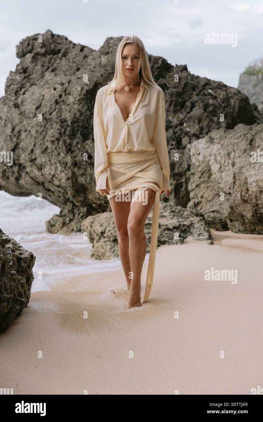 Una donna bionda cammina tra le rocce costiere su una spiaggia sabbiosa Foto Stock