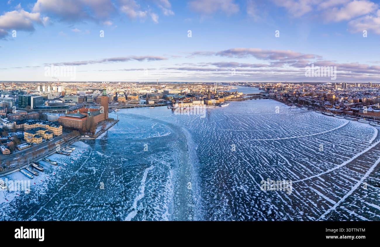 Vista aerea delle acque ghiacciate che riflettono la luce soffusa dell'inverno, abbracciando l'iconico Municipio di Stoccolma, mentre la città si risveglia con un fascino gelido, sto Foto Stock