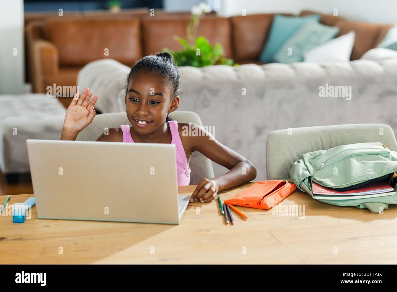 Computer portatile argentato e forniture scolastiche colorate sono seduti su un tavolo di legno vicino al divano e allo studio domestico Foto Stock