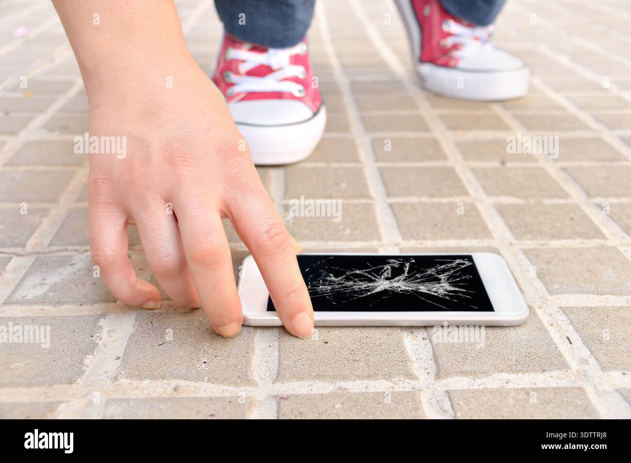 Persona che sceglie uno smartphone rotto con uno schermo del terreno incrinato Foto Stock