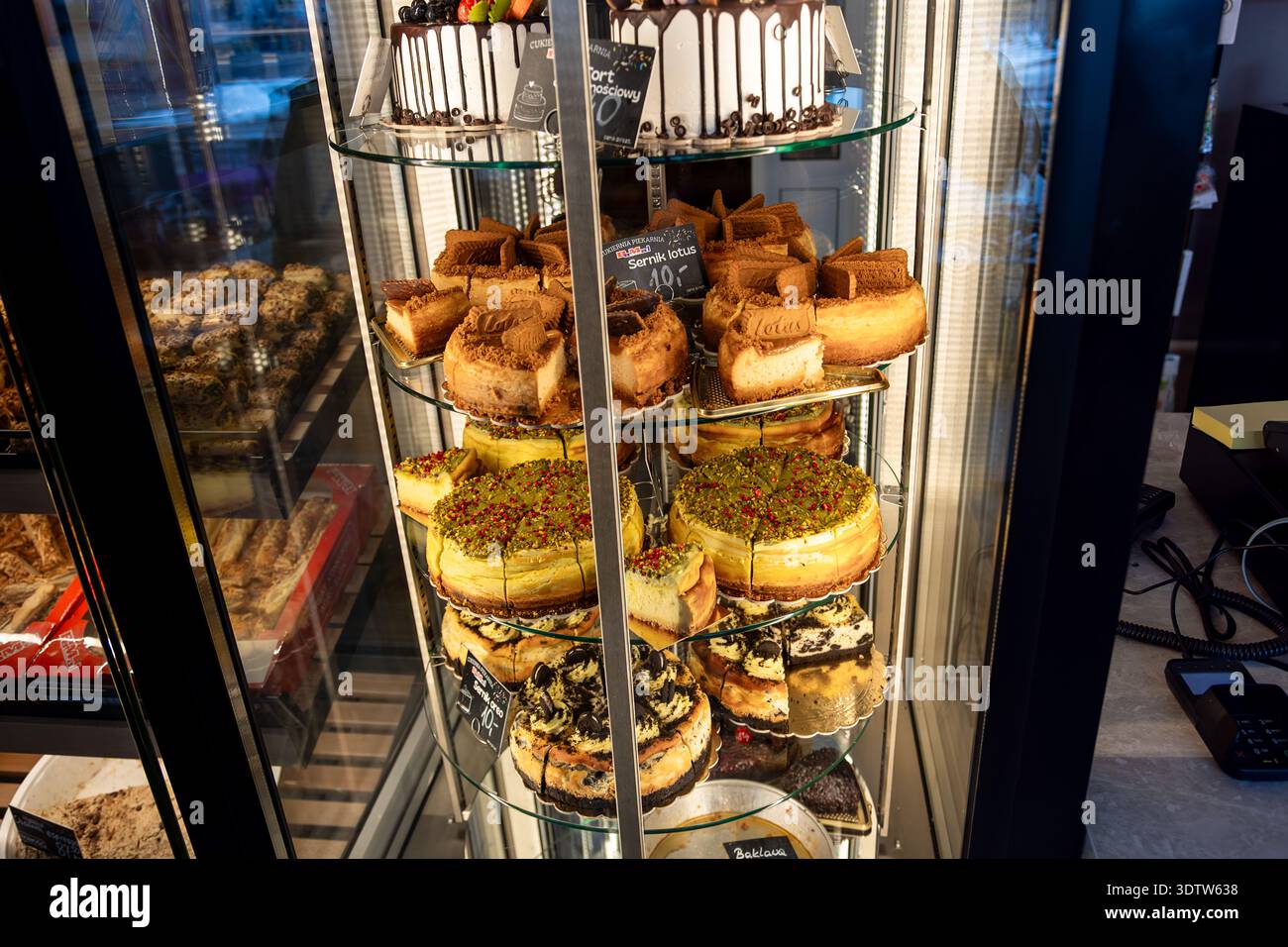 Cheesecake e torte assortite in una vetrina di vetro refrigerata in una panetteria o caffetteria, tra cui varietà di pistacchio, Oreo e Biscoff. Foto Stock