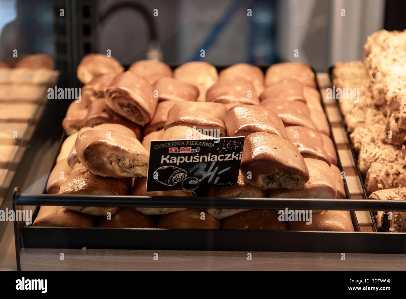 Pasticcini di cavolo polacchi (kapuśniaczki) in un vassoio da forno con il cartello del prezzo, salati prodotti da forno in vendita in una pasticceria. Foto Stock