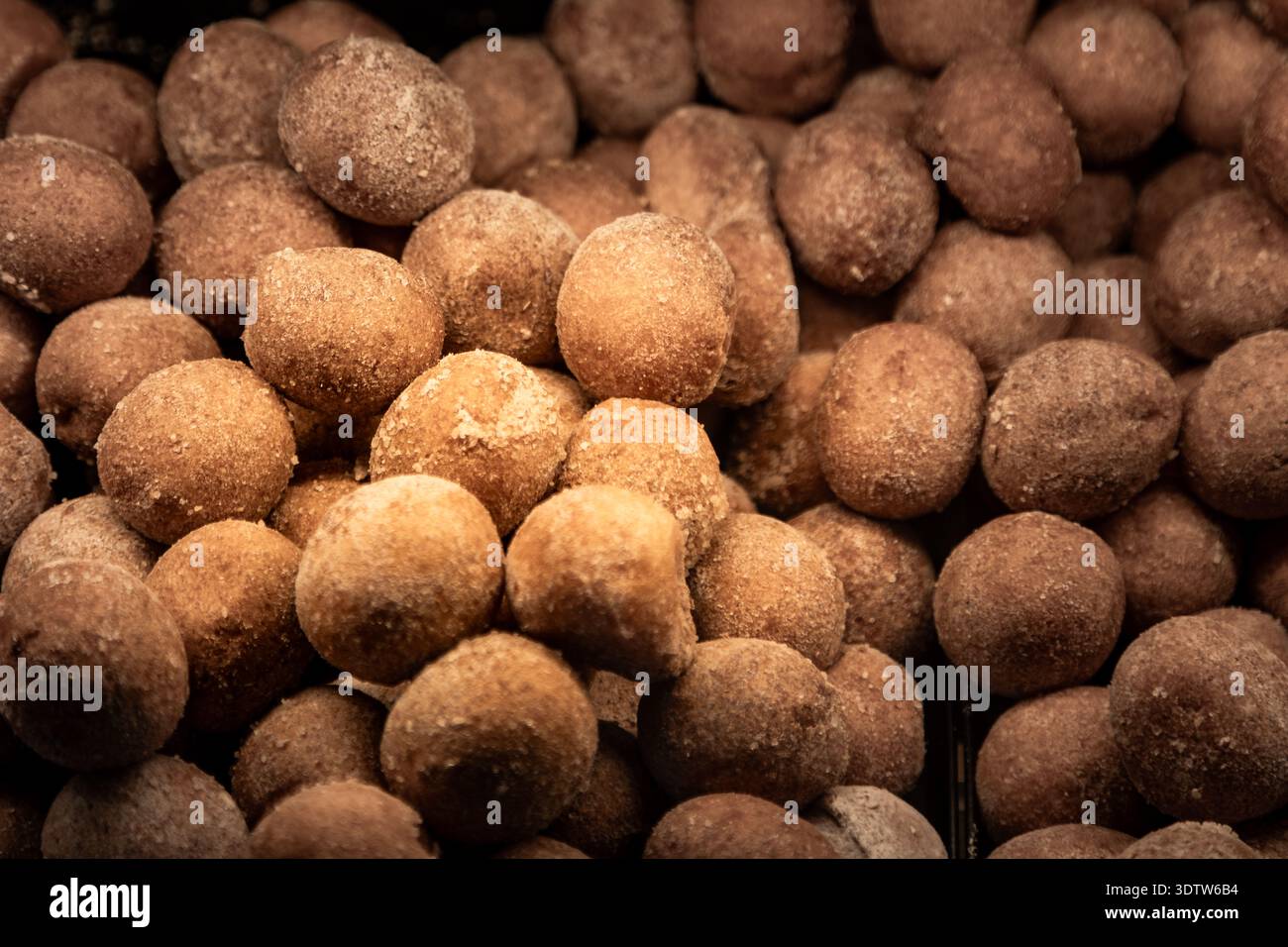 Mini fori di ciambelle ricoperti di zucchero esposti in una vetrina di panetteria, dolci freschi in vendita in una pasticceria o in un caffè. Foto Stock