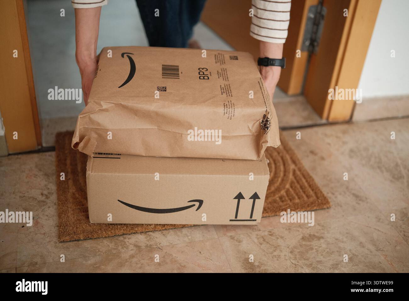 Alicante, Spagna - 2 febbraio 2026: Ricezione di ordini online Amazon a casa. Consegna Amazon prime. Donna che prende gli oggetti consegnati all'ingresso di casa Foto Stock