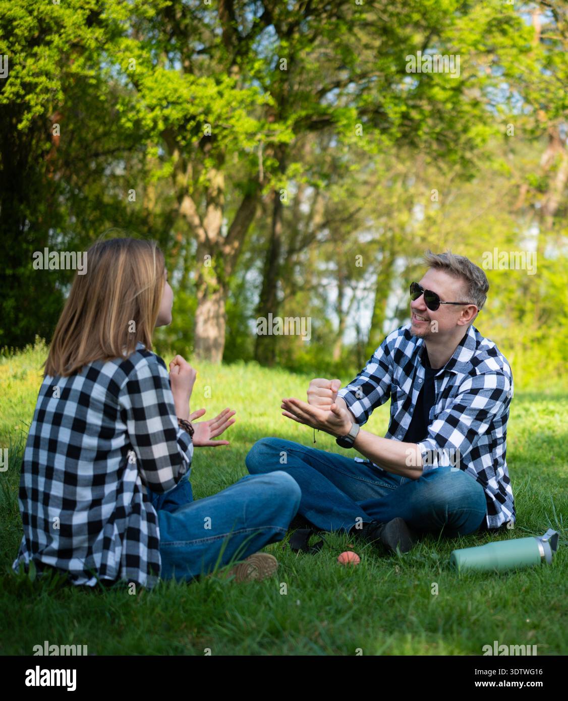 Padre e figlia seduti su Grass in Summer Park suonano Rock Paper Scissors Foto Stock