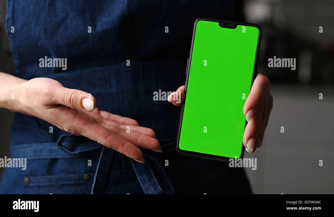 Ragazza con grembiule che tiene in mano Uno smartphone Chroma Key Greenscreen Foto Stock