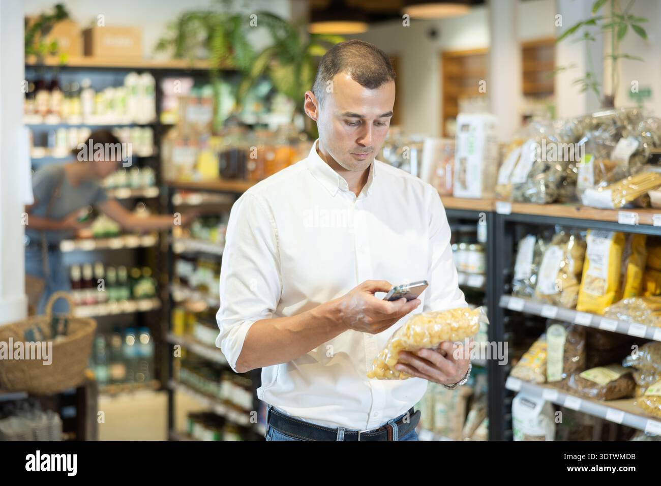 Uomo che scansiona un sacchetto di pasta con smartphone nel negozio di alimentari Foto Stock