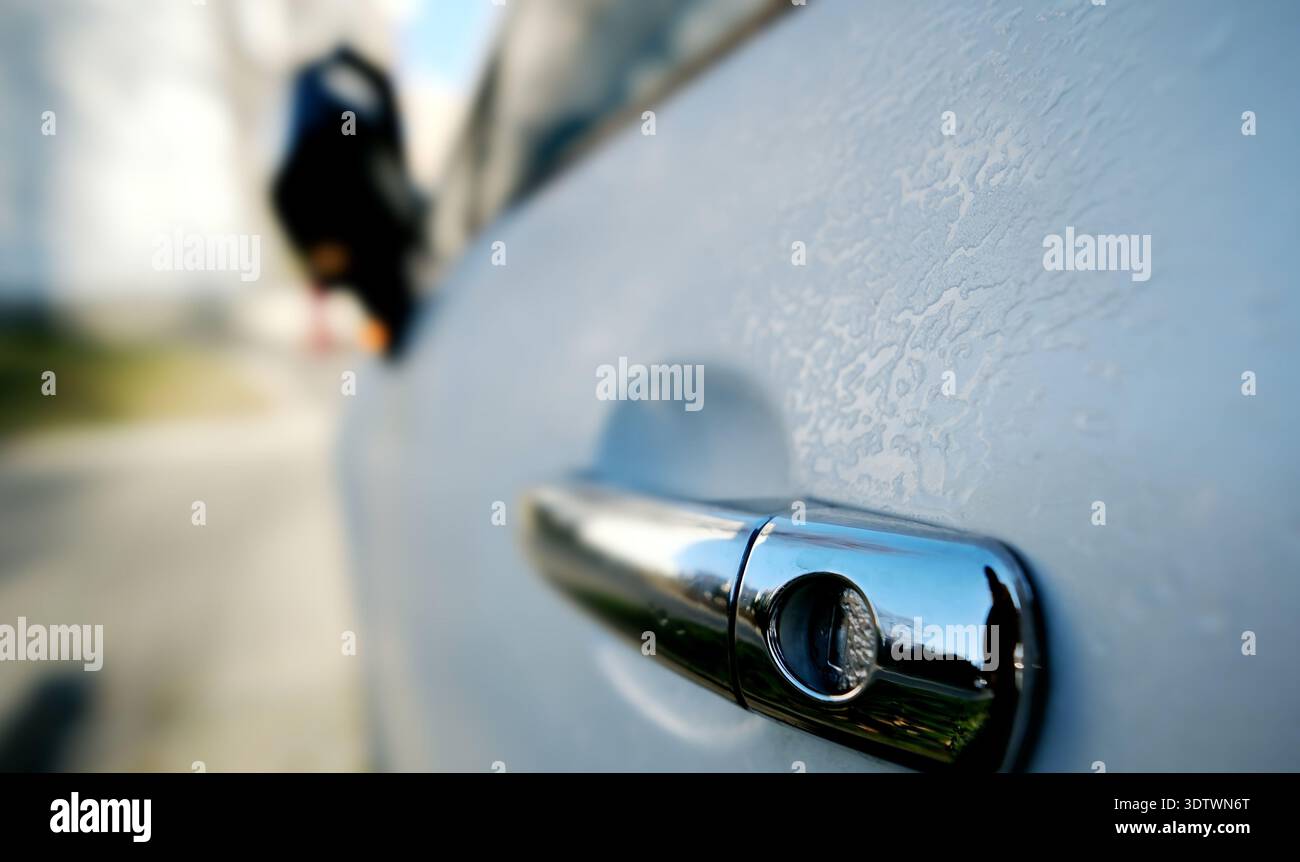 Maniglia della porta lato guida dell'auto coperta dal gelo nel parcheggio con luce del mattino Foto Stock