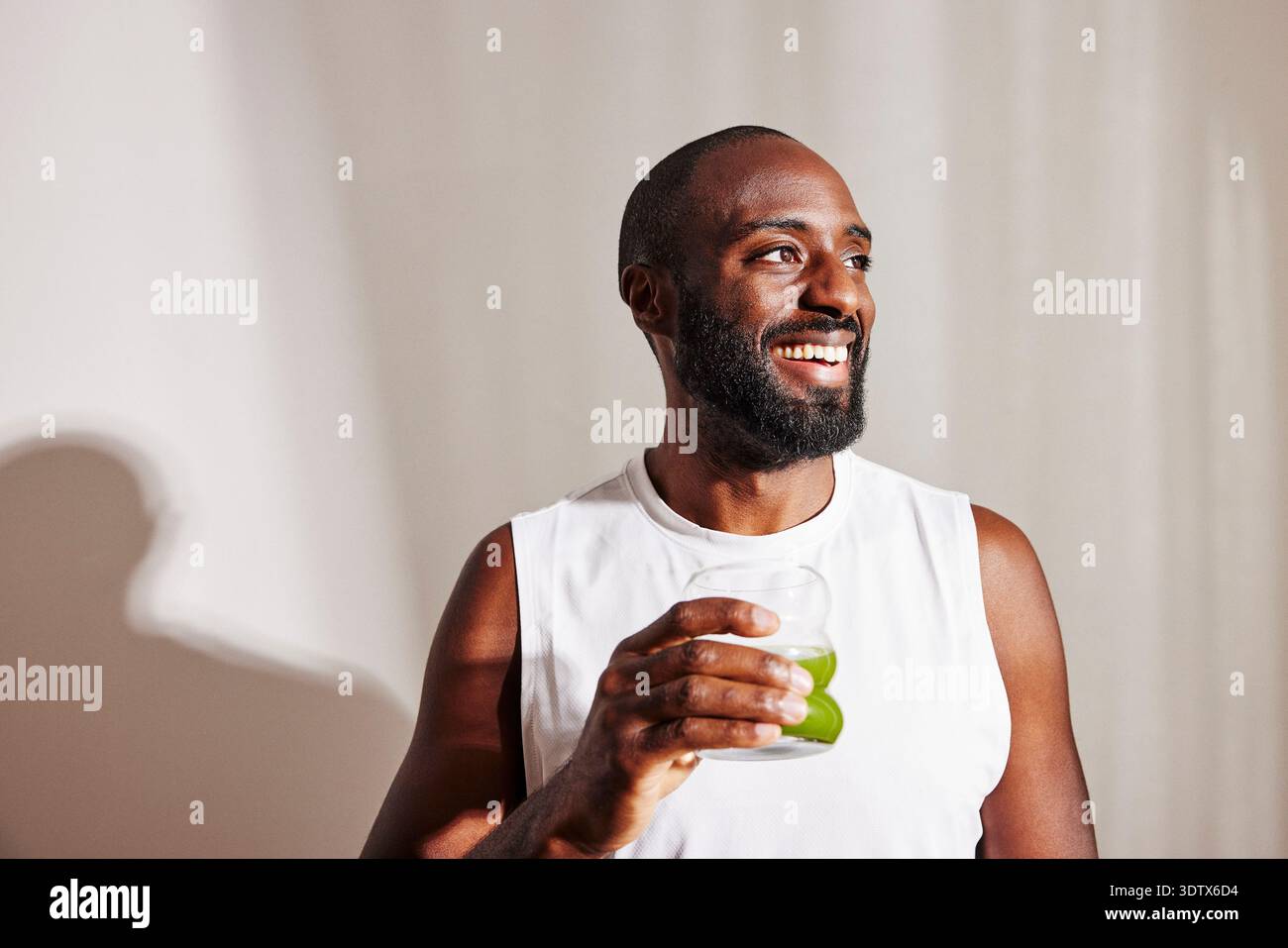Uomo sorridente con barba che guarda lontano tenendo in mano il bicchiere per succo di disintossicazione Foto Stock