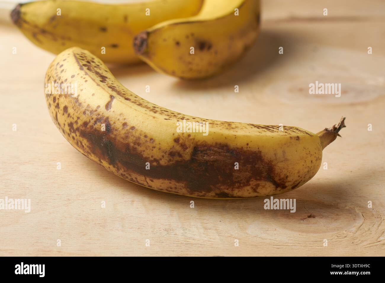 banana gialla ultrapura su superficie in legno ruvido chiaro, frutta con macchie di pelle nere, primo piano messa a fuoco morbida con spazio di copia, consapevolezza degli sprechi alimentari Foto Stock