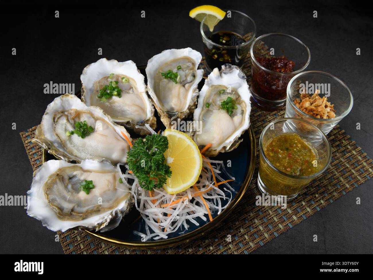 Un piatto di ostriche fresche servite su daikon grattugiato con condimenti assortiti, tra cui salsa di pesce, scalogni fritto e pasta di peperoncino Foto Stock