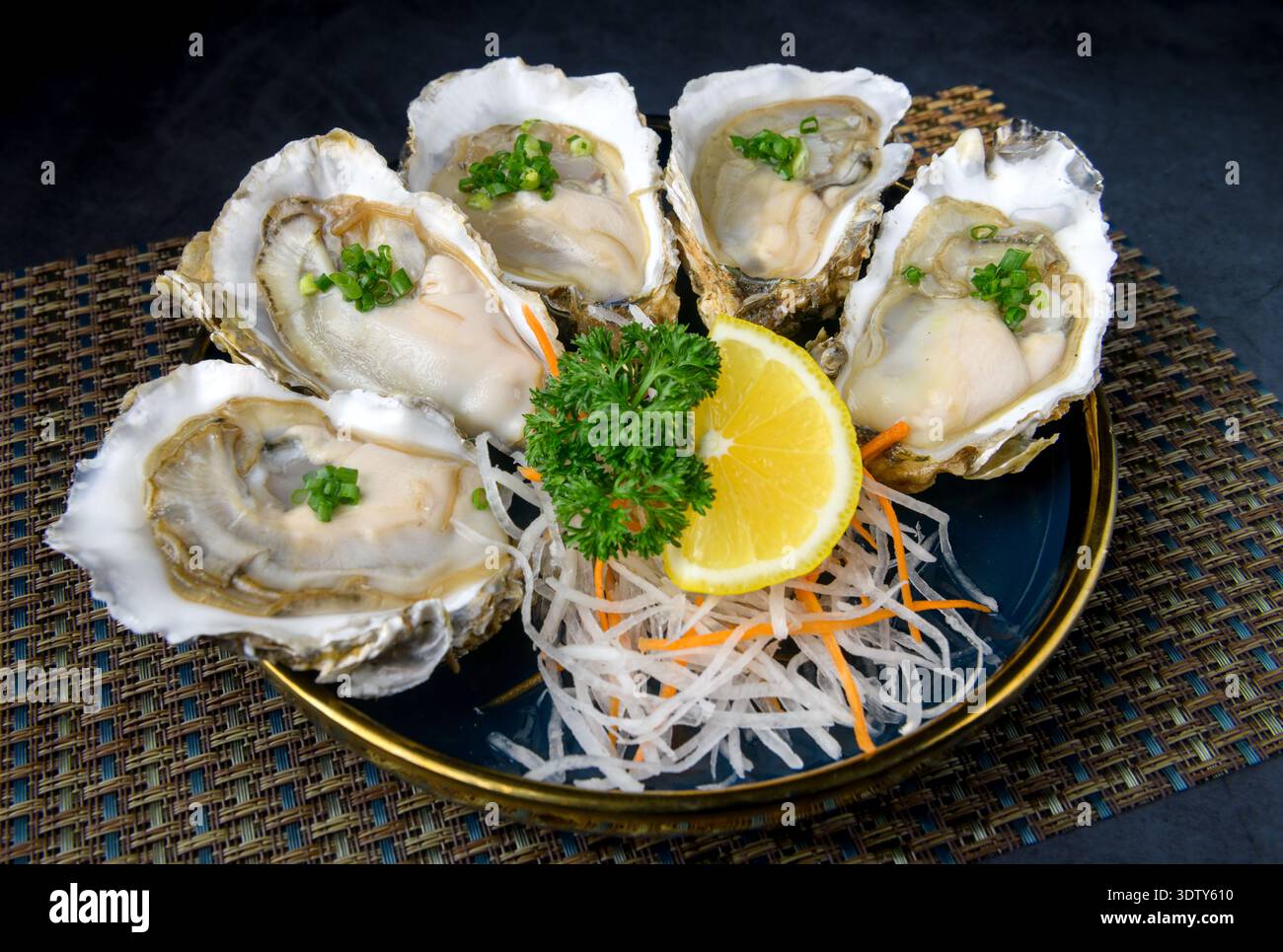 Un piatto di ostriche fresche servite su daikon grattugiato con condimenti assortiti, tra cui salsa di pesce, scalogni fritto e pasta di peperoncino Foto Stock