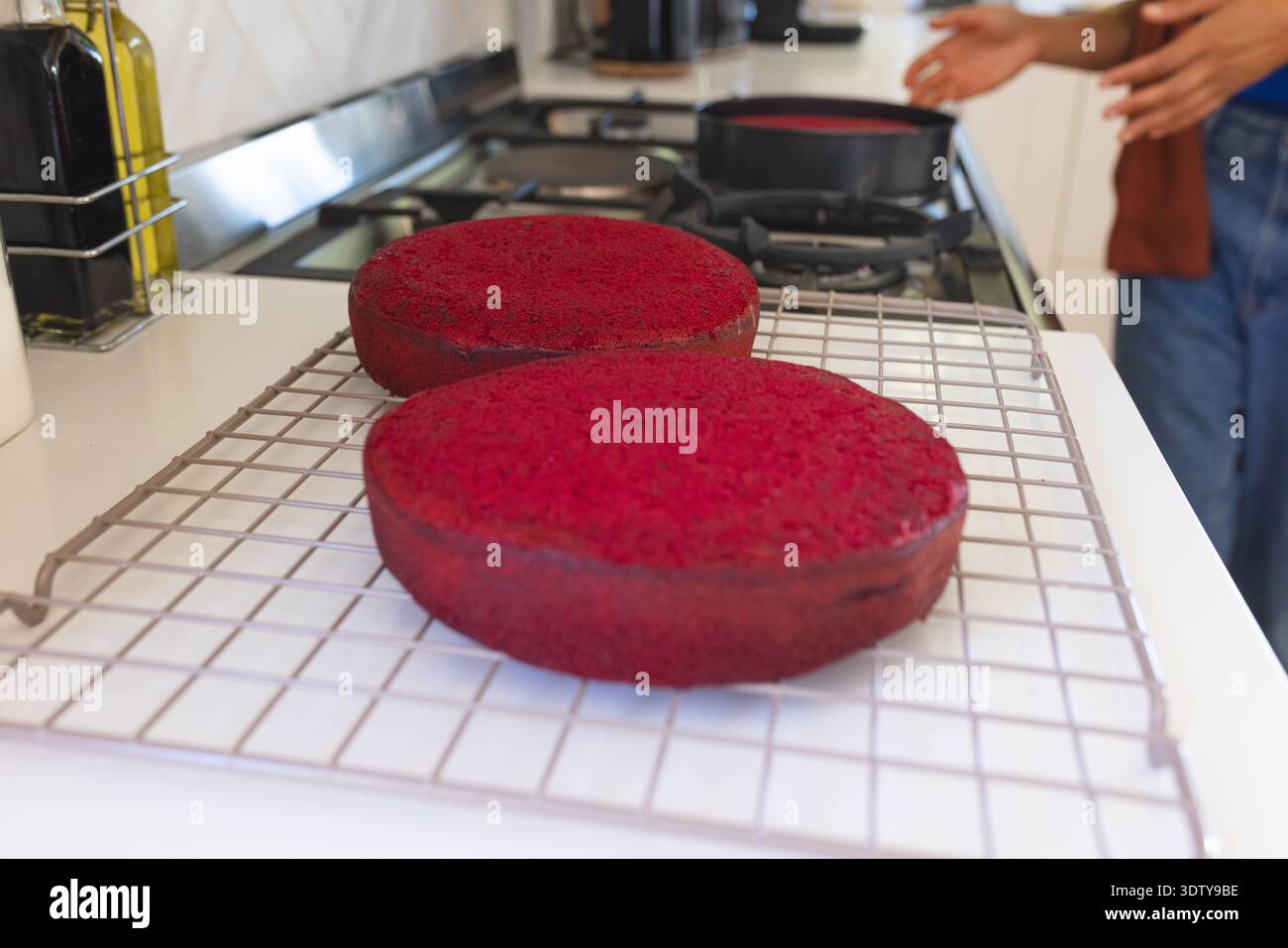 Due strati di torta rossa si raffreddano su una griglia metallica sul piano di lavoro bianco nella cucina domestica Foto Stock