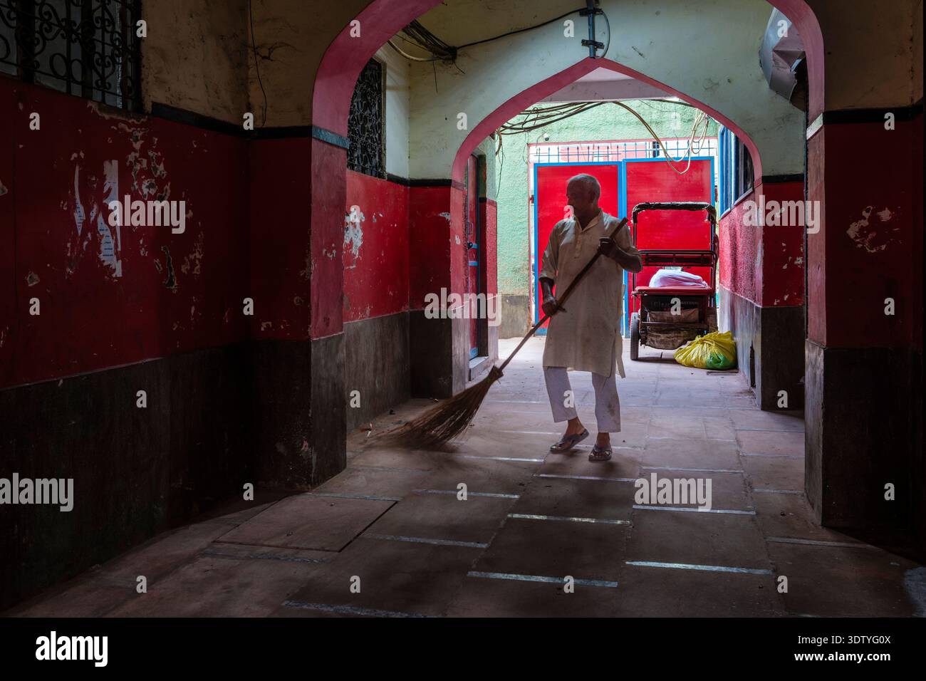 Un uomo spazza un pavimento piastrellato con una scopa tradizionale all'interno di un passaggio pedonale ad arco vicino all'affollato Chandni Chowk nella Vecchia Delhi. Foto Stock