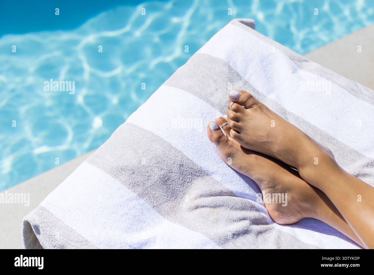 Donna afroamericana che riposa le gambe mostrando unghie dipinte su un asciugamano grigio a bordo piscina, spazio copia Foto Stock
