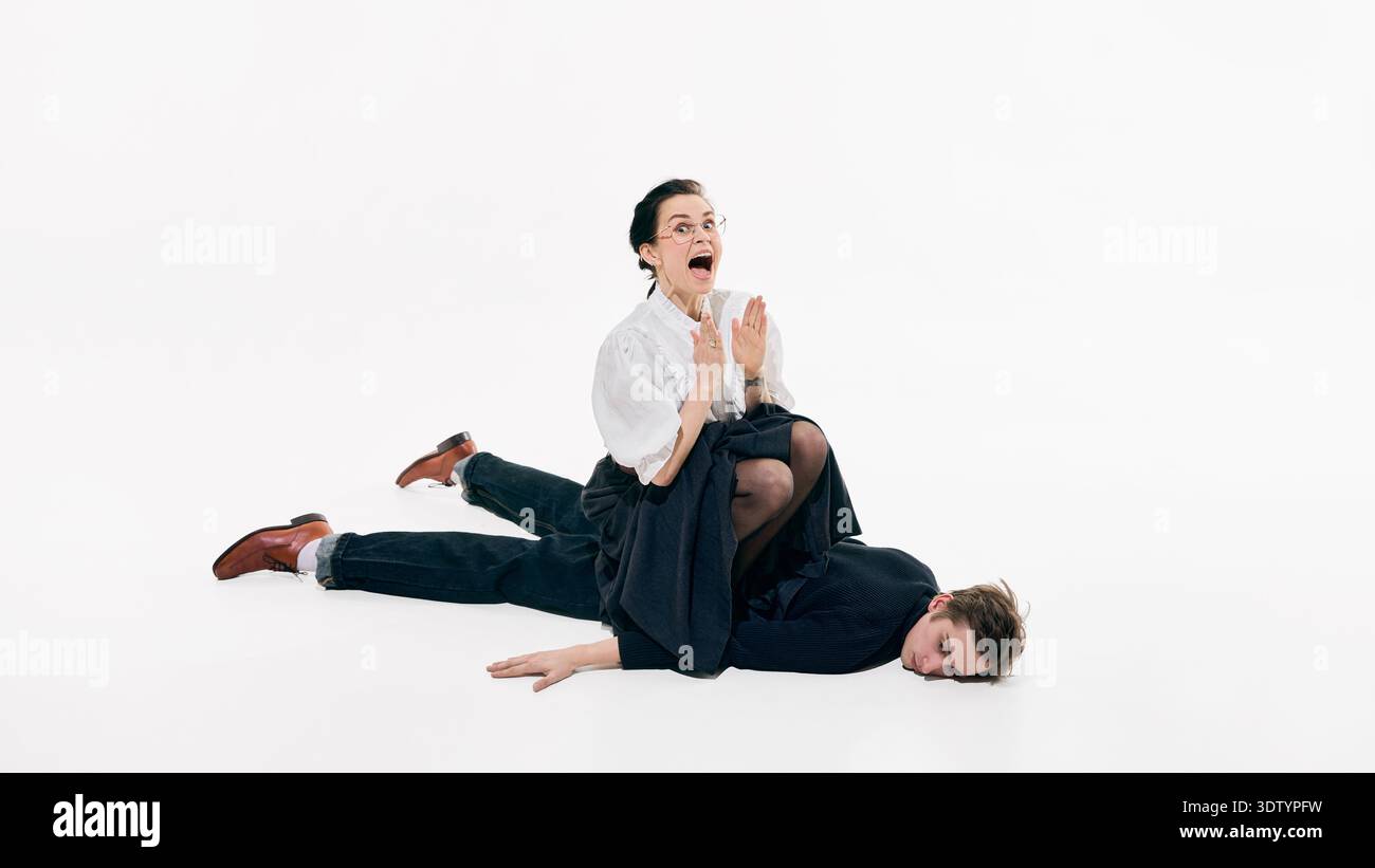 Donna seduta su un uomo sdraiato sul pavimento dello studio in una giocosa composizione di moda d'affari Foto Stock
