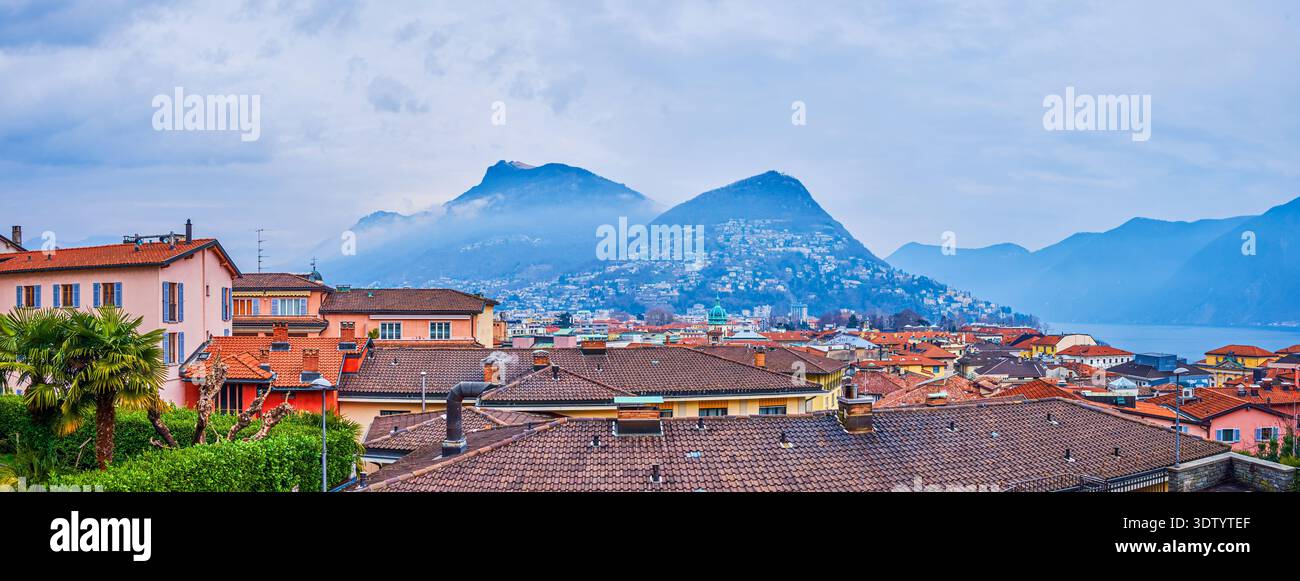 vista panoramica delle montagne dietro i tetti storici urbani di Lugano, Svizzera Foto Stock