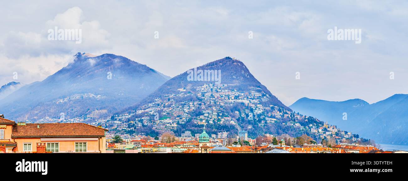 vista panoramica delle montagne dietro i tetti storici urbani di Lugano, Svizzera Foto Stock