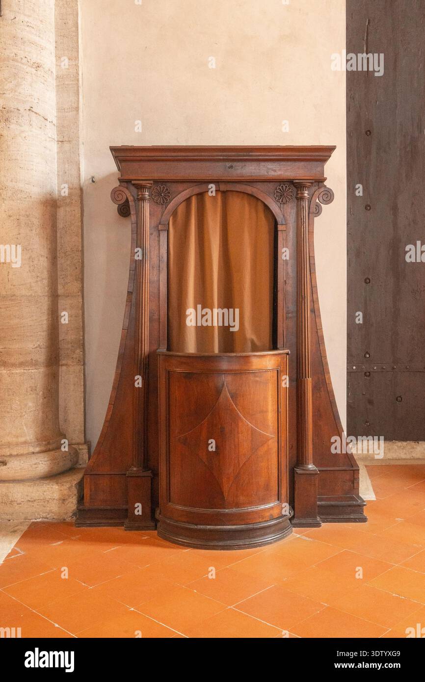 Confessionale in legno intagliato contro il muro di pietra. Elemento storico della chiesa che mette in risalto l'artigianato e l'architettura culturale. Foto Stock