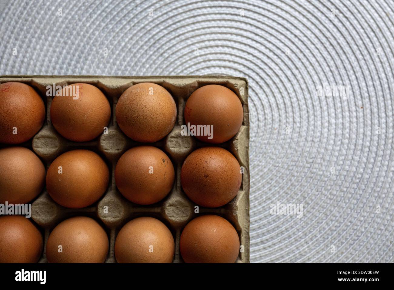 Una vista pulita e minimalista dall'alto verso il basso (piatto) delle uova di pollo marrone fresche accoccolate in un cartone grigio. Il cartone è collocato su un moderno, argento, Foto Stock