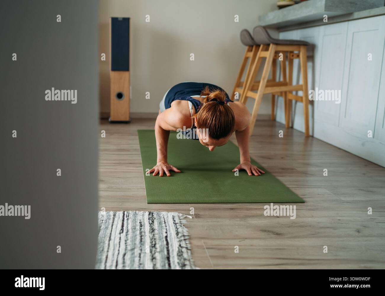 Giovane donna motivata e sana che mantiene una posizione forte sul suo tappetino verde, concentrandosi sulla forza del nucleo durante uno yoga a casa e il fitness Foto Stock