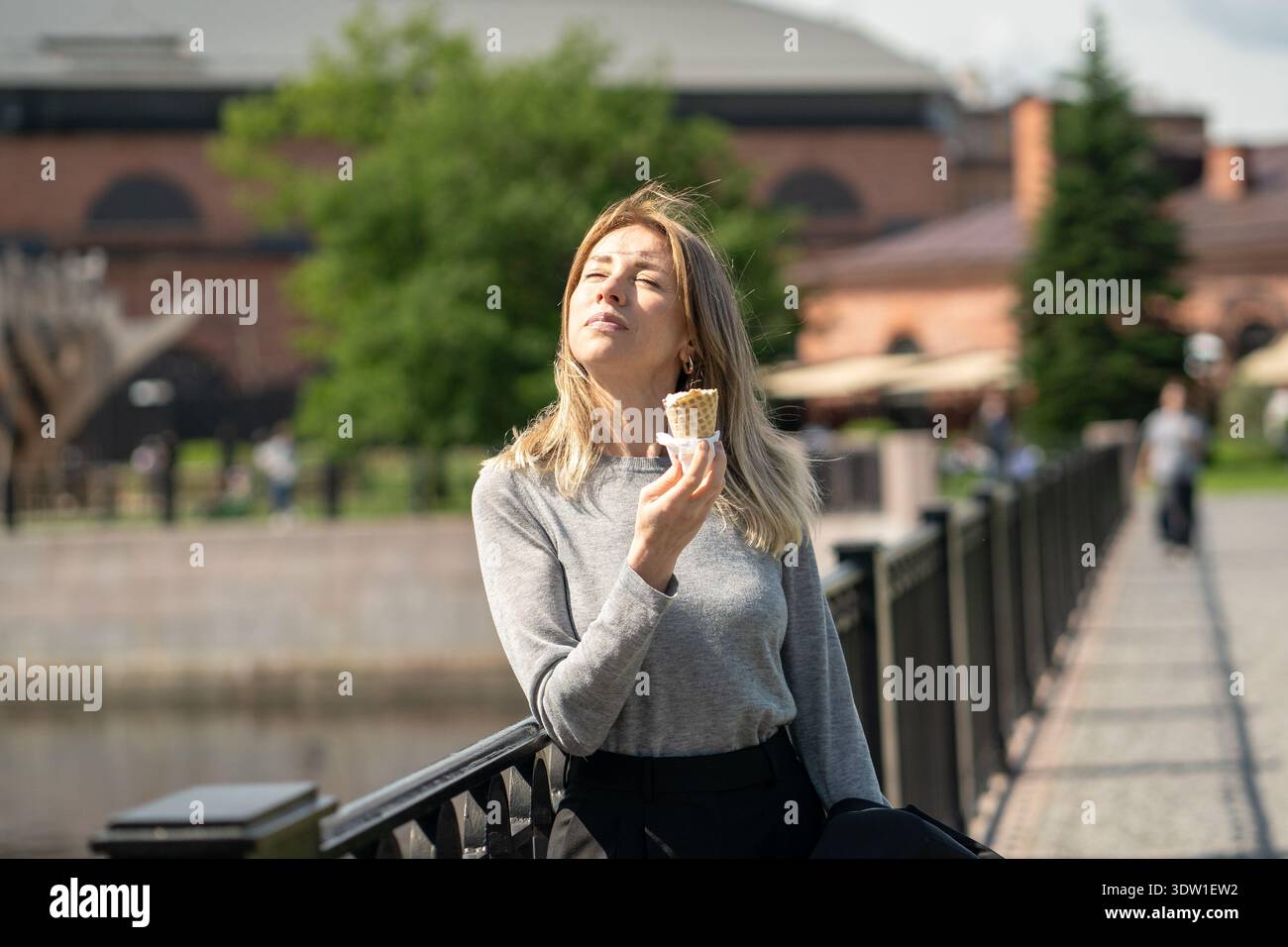 Una donna d'affari spensierata ama le giornate soleggiate e i gelati, si erge sul ponte a picco sul sole Foto Stock