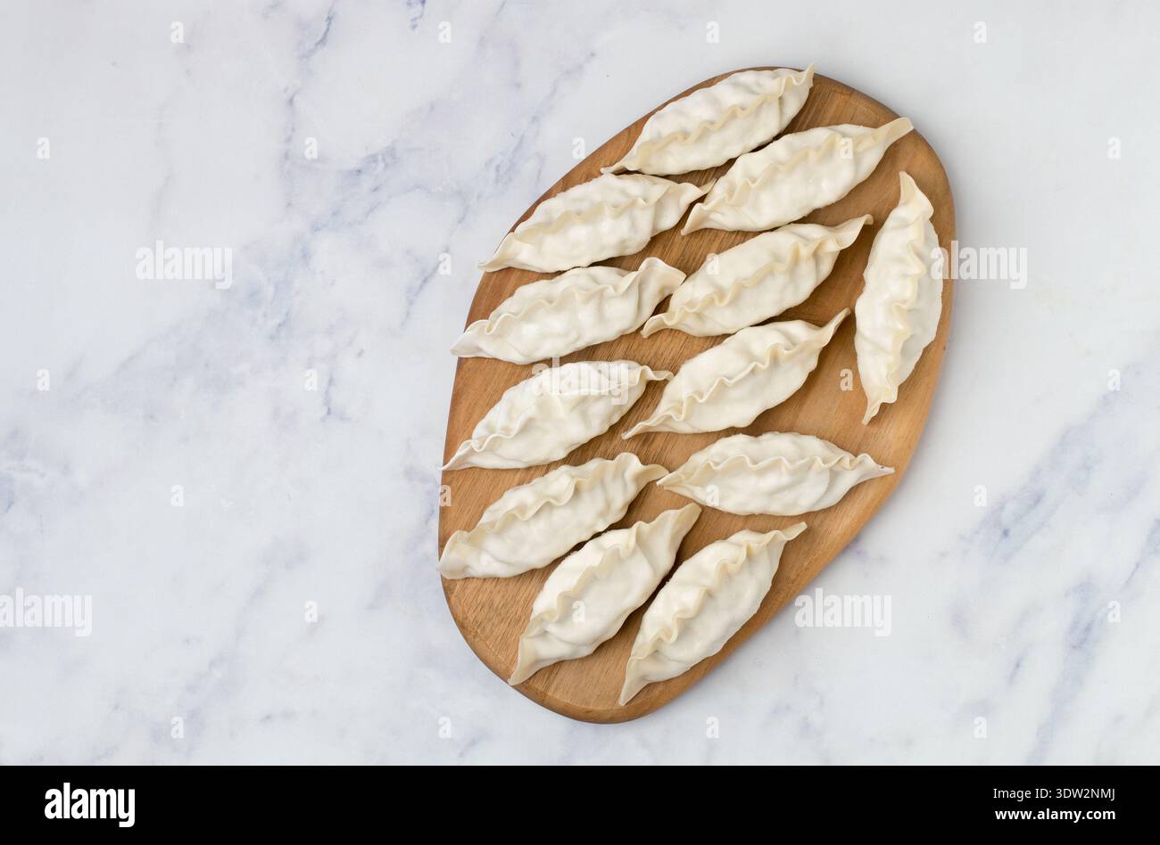 Gyoza crudi su un asse di legno. Messa a fuoco selettiva, vista dall'alto Foto Stock