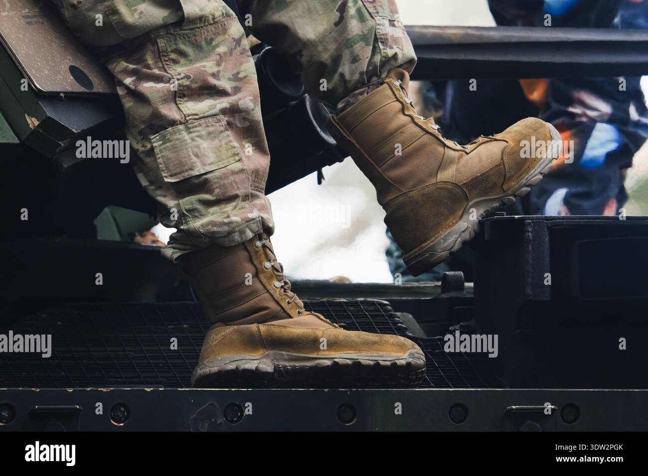 Primo piano di un soldato con pantaloni mimetici e stivali tattici da deserto seduti su un veicolo blindato durante una missione militare. Foto Stock