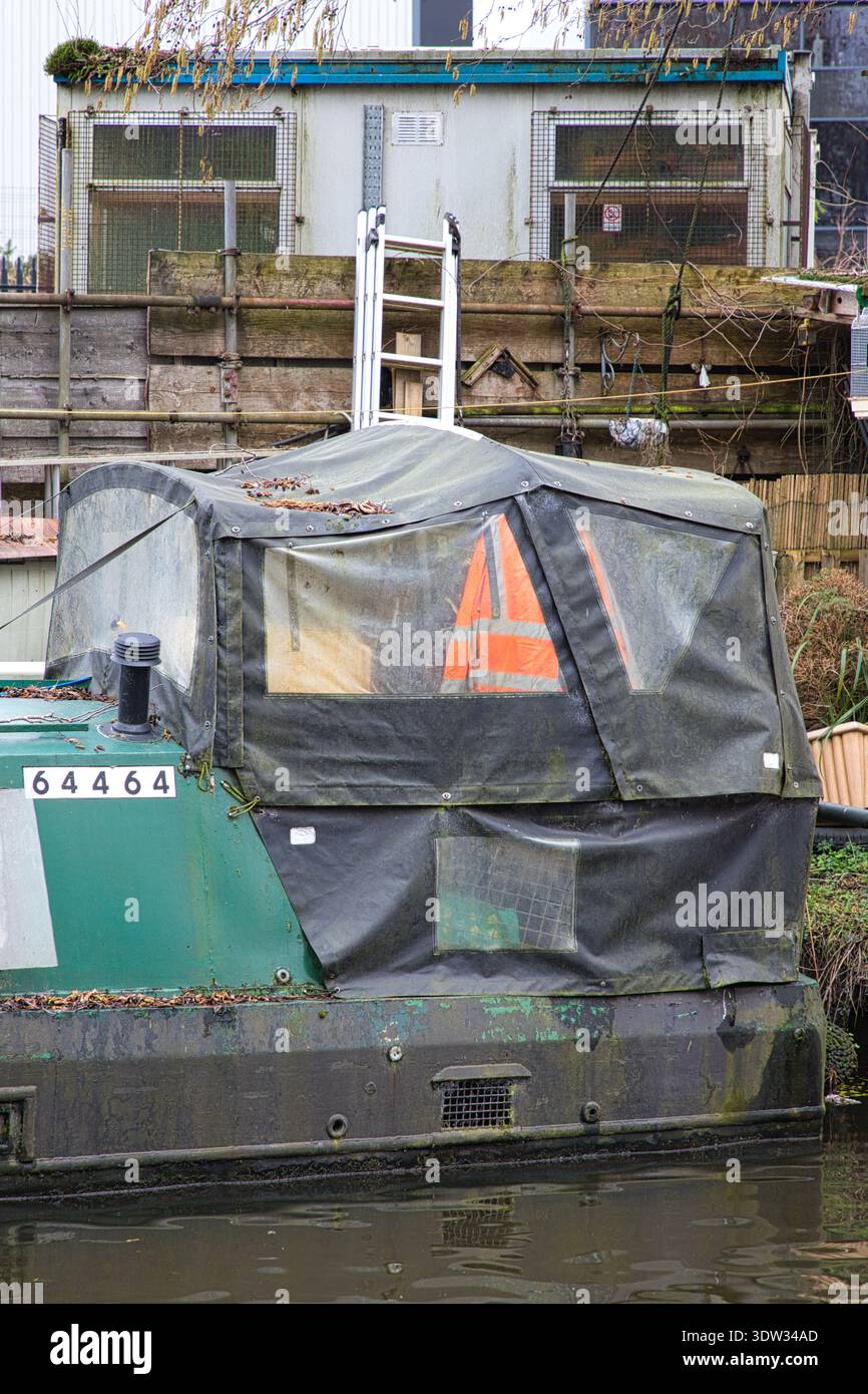 Primo piano di una barca stretta ormeggiata sul Peak Forest Canal, Tameside, Regno Unito, con una copertura in tela nera e una giacca ad alta visibilità all'interno. Foto Stock