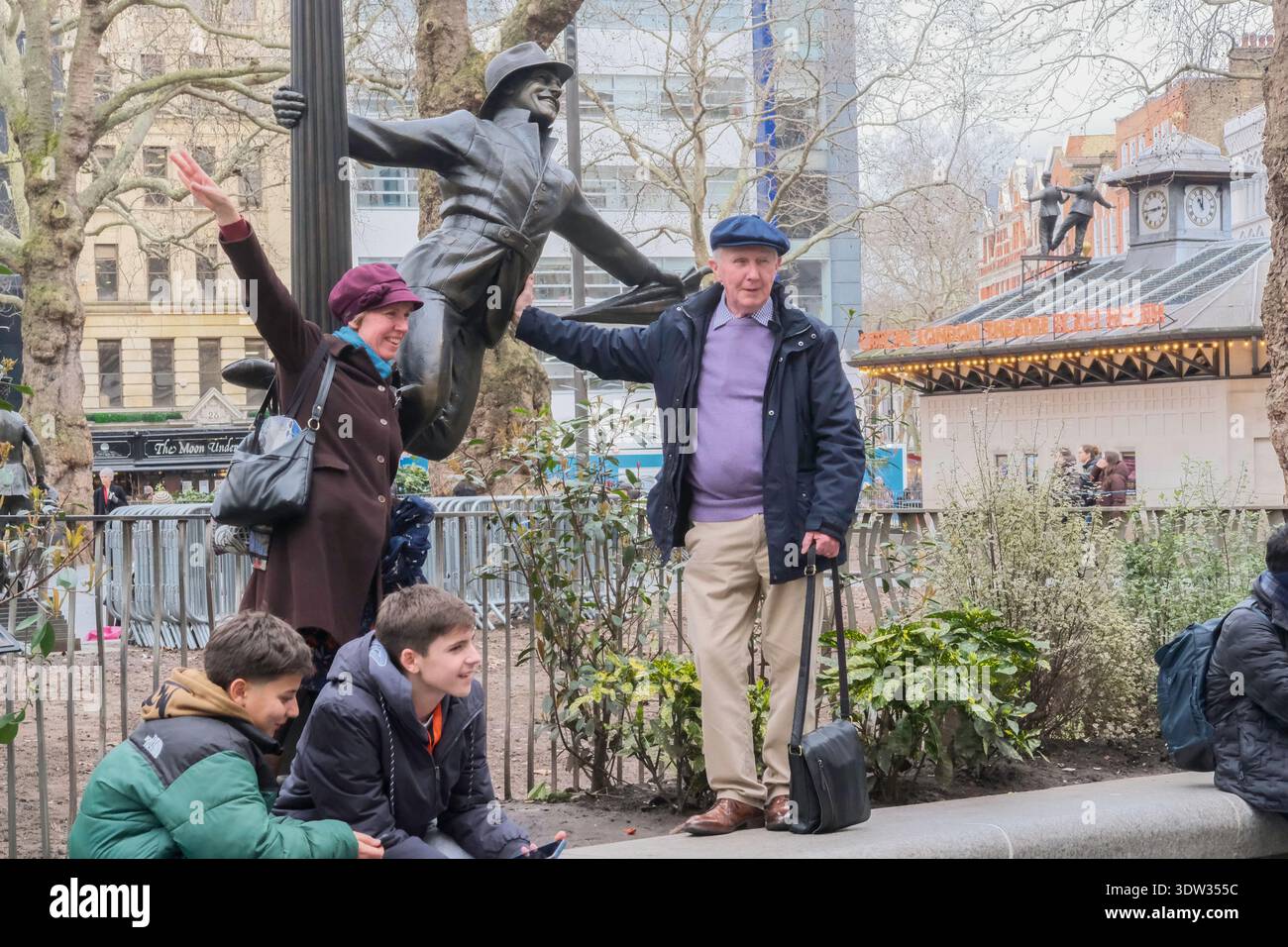 La gente posa con la statua di Gene Kelly di Singing in the Rain, uno dei film iconici celebrati in Scenes in the Square, Leicester Square, Londra. Foto Stock