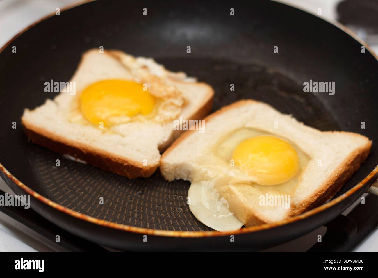 Primo piano di due uova in un cestello, noto anche come rospo nel buco, frittura in una teglia nera antiaderente. I tuorli gialli crudi si trovano al centro del pane bianco. Foto Stock